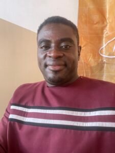 Portrait of a person wearing a maroon sweatshirt with white and black horizontal stripes, seated against a two-toned wall with taupe and orange sections