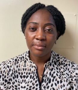 A woman with dark, braided hair and a patterned blouse looks directly at the camera