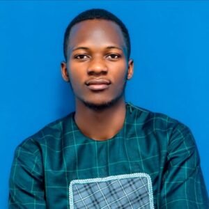 A young man with short hair and a plaid shirt looks directly at the camera against a blue background
